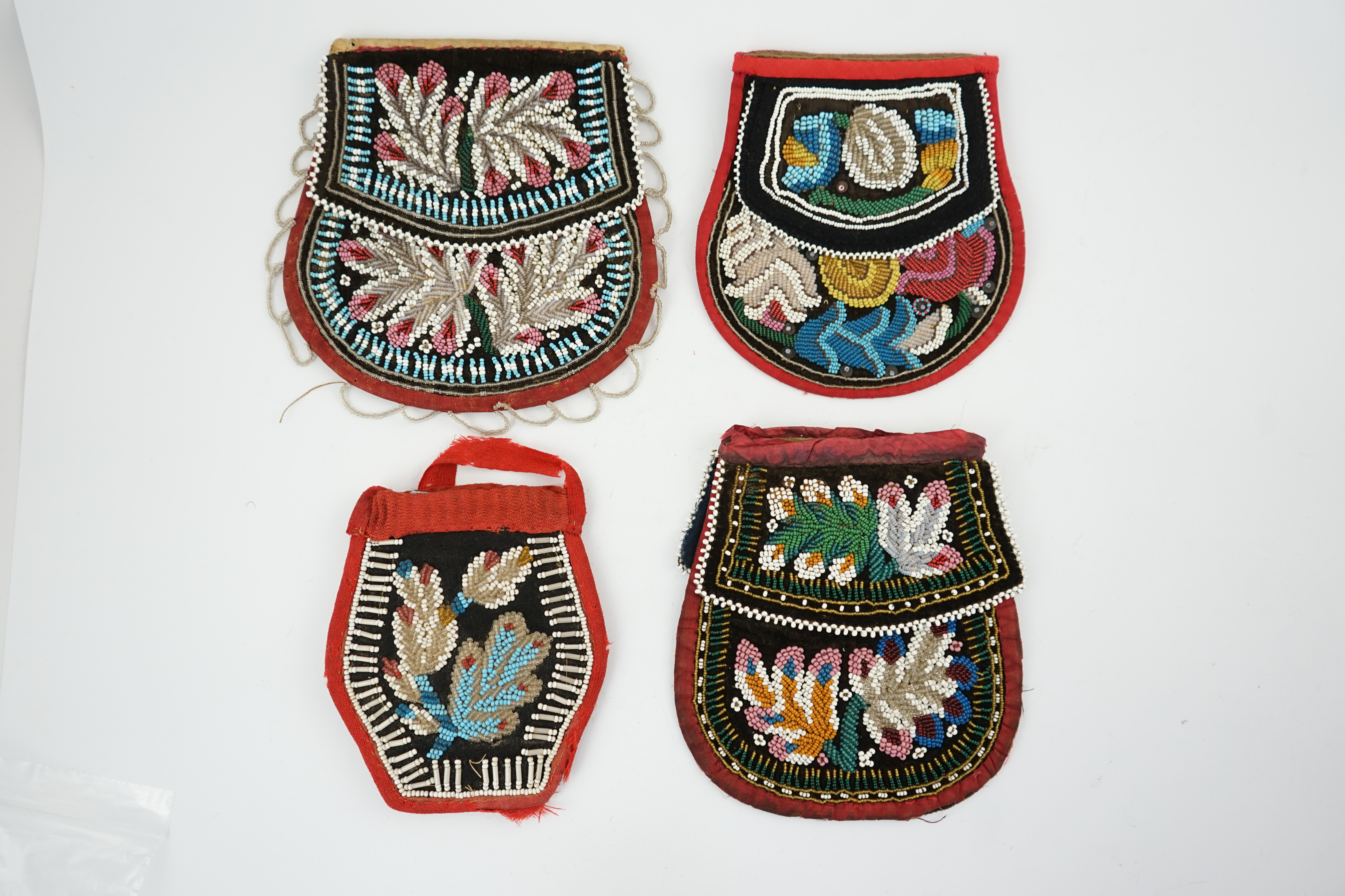 Three 19th century Iroquois Native American beaded bags and a smaller pouch, the bags have beaded flaps, the pouch is shaped with mostly white and turquoise beading having a red fabric edging, all four have very differen